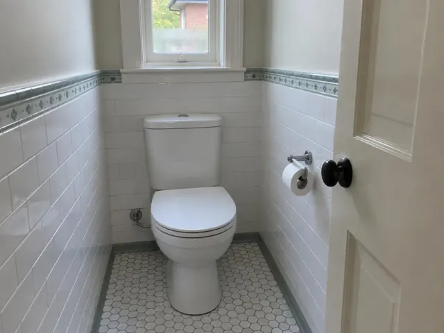 Clean white toilet in a tiled bathroom with patterned floor and window in Waitara