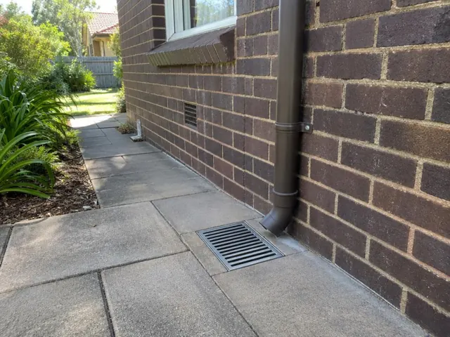 Outdoor drain grate beside a brick house and paved path in Hornsby