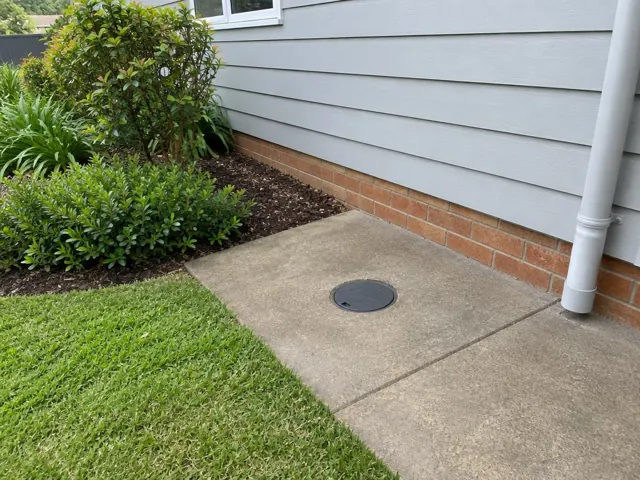 Capped access cover in a concrete slab beside a weatherboard house and garden in Mount Colah